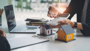 man holding calculator with wooden house models on a table